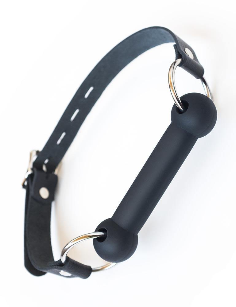 The Kinklab Silicone Bit Gag With A Leather Strap is shown against a blank background. The gag bit is made of matte black silicone and attached to the leather head strap with metal O-rings. 