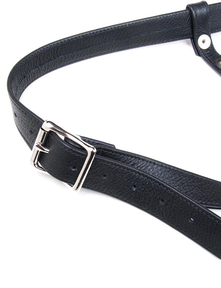 A close-up of the hip strap of the black leather Buzz Me Tender strap-on harness is shown against a blank background. The strap is adjustable and fastens with a metal buckle.