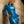 Load image into Gallery viewer, A blonde woman leans against a tan brick wall with her hand on her hip. She wears the long sleeve Latex Mistress Dress from Syren Latex in pearl blue. The dress is form-fitting and has a turtleneck, and the hem cuts off at her mid-thigh. 
