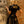 Load image into Gallery viewer, A blonde woman wearing the Ruffly Latex Rubber Heidi Dress in black by Syren Latex stands facing a brick wall. The dress has an invisible zipper down the back. The hem ends at her mid-thigh.
