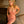 Load image into Gallery viewer, A blonde woman poses in a stairwell wearing the Latex Ruffled Boobie Dress from Syren Latex. The dress is transparent pink with gold ruffle accents on the shoulders and neck. The dress has a collar and a cutout above the bust.
