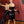 Load image into Gallery viewer, A bald woman, holding a flogger in her hand and wearing the Newmar Latex Dress in black with a black waist cincher, stands in front of a man tied to a St. Andrews cross. On the wall behind her are various other BDSM implements. 
