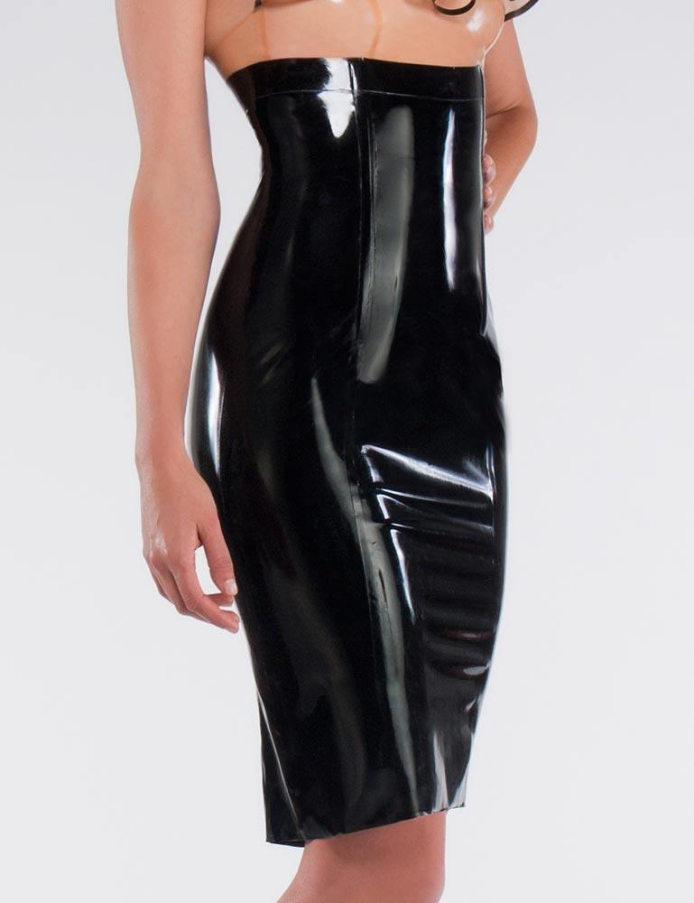 A woman poses in front of a grey backdrop. She is wearing a tan latex Jabot Top with black accents and the form-fitting latex Empire Waist Pencil Skirt in black from Syren Latex.