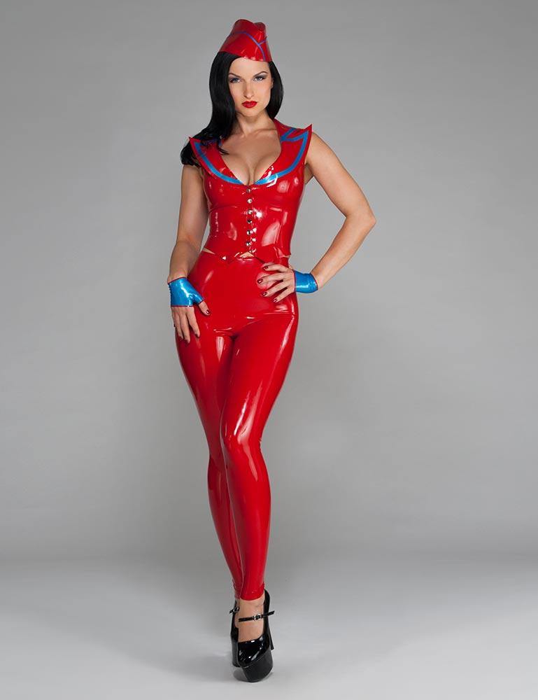 A woman with black hair and red lipstick poses in front of a grey backdrop, wearing the Natural Waist Leggings by Syren Latex in red. She also wears a matching top with blue trim, a matching latex hat, and blue latex glovelettes.