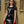Load image into Gallery viewer, A brunette woman with red lipstick leans against a brown wall, wearing The Jane Latex Dress by Syren Latex in black, as well as a black waist cincher and red latex driving gloves. The dress has a scoop neck and short sleeves.
