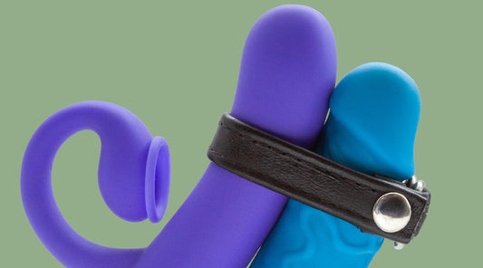 A purple vibrator held against the shaft of a blue dildo with a black leather C-ring.