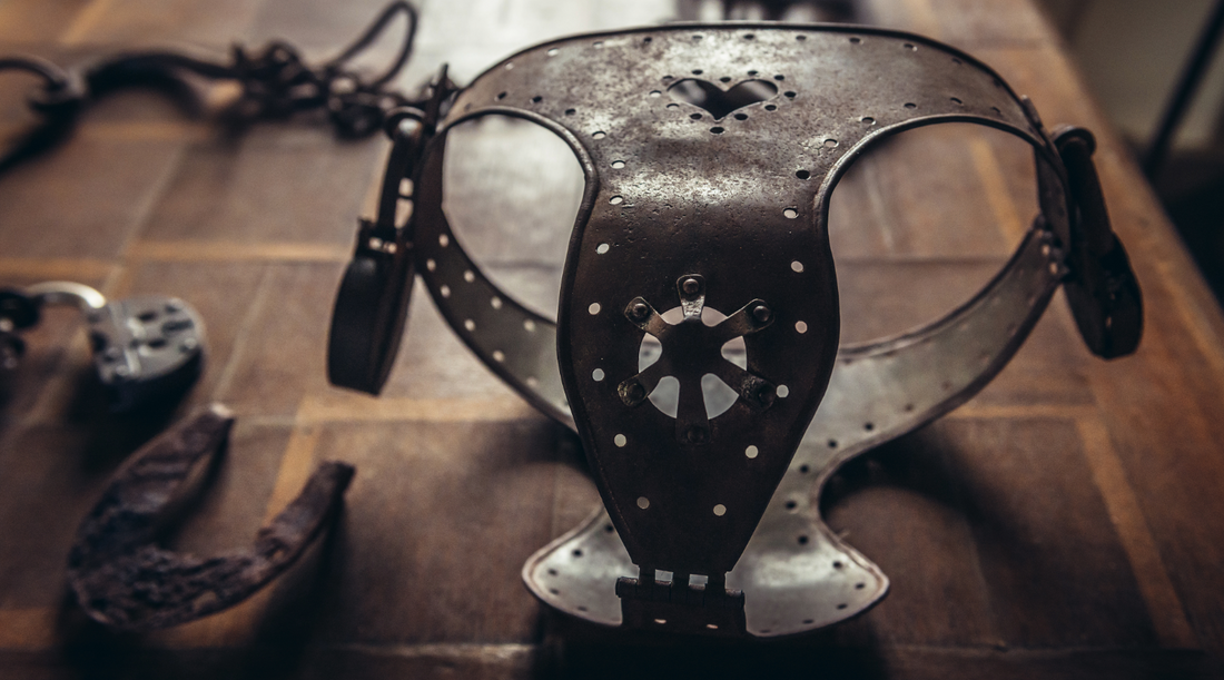 A wooden table with a collection of ancient devices, with a rusted metal "chastity belt" at the center.