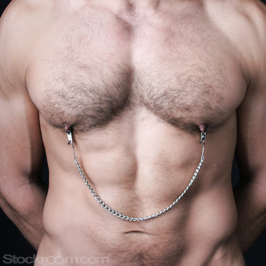 A close-up of a muscular man’s bare torso with some body hair is shown. He wears the silver Mini Nipple Clamps.