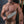 Load image into Gallery viewer, A close-up of a nude man’s hairy chest is shown. He holds the Black Leather Fraternity Paddle in his fist in front of his chest.
