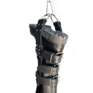 An upside black leather boot with Boot Suspension Cuffs on it is shown against a blank background. The cuffs have a leather strip running down the leg with three buckles around the leg. A carabiner clips to the D-rings at the end of the strips.