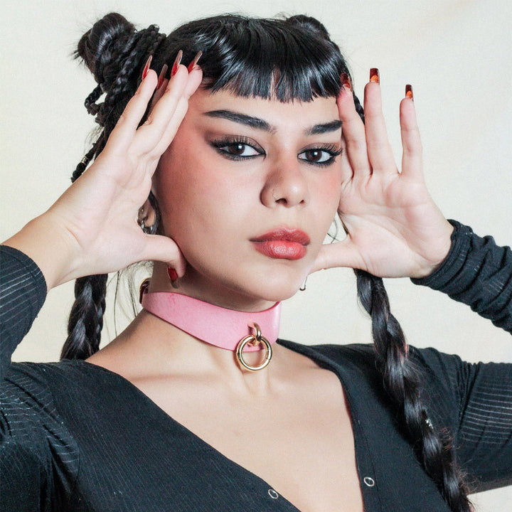 A young woman with short black bangs and long braids wearing the Luxury leather Day Collar in pink.