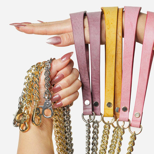 A collection of luxury Italian leather leashes in dusty pink, mustard yellow, and deep mauve, displayed on a model’s hand. Each strap features silver or gold metal chain links with matching lobster clasps. The textured leather and sturdy metal hardware enhance durability and style.
