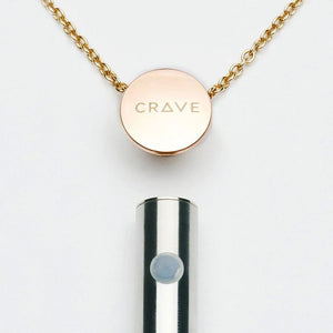 The bottom of the Vesper Pendant Necklace Vibrator is shown below a rose gold chain, which has a pendant with the Crave logo on it. The vibrator has one small button.