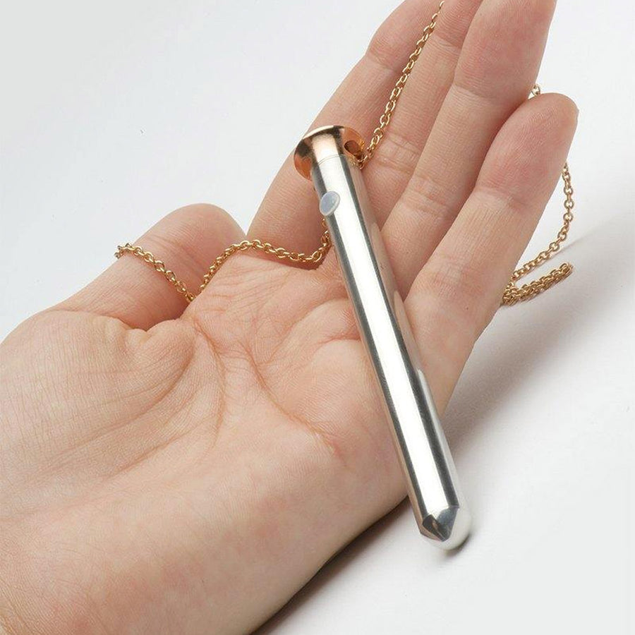 A hand is shown holding the Vesper Pendant Necklace Vibrator in Rose Gold against a blank background.