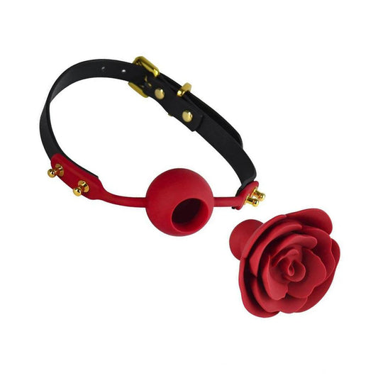 The Rose Ball Gag is displayed taken apart against a blank background. The gag has a leather strap with gold hardware and a red silicone ball in the center with a hole. A red silicone rose with a plug in the back is in front of the gag.