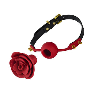 The Rose Ball Gag is displayed taken apart against a blank background. The gag has a leather strap with gold hardware and a red silicone ball in the center with a hole. A red silicone rose with a plug in the back is in front of the gag.