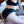Load image into Gallery viewer, A person wearing a black fabric bra and the Em.Ex. Silhouette Crotchless Strapon Harness is shown from the back kneeling on a bed. They are holding hands with another person infront of them who is wearing white lingerie.
