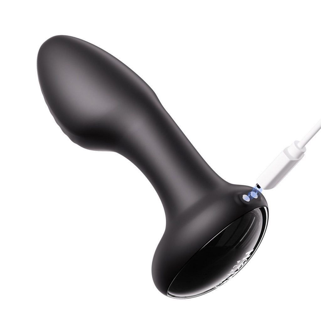 Black model of the Frenzy Butt Plug tilted away from the viewer to show the two charging holes. A white cord comes from the right side, with illustrated electrical current connecting it to the charger. 