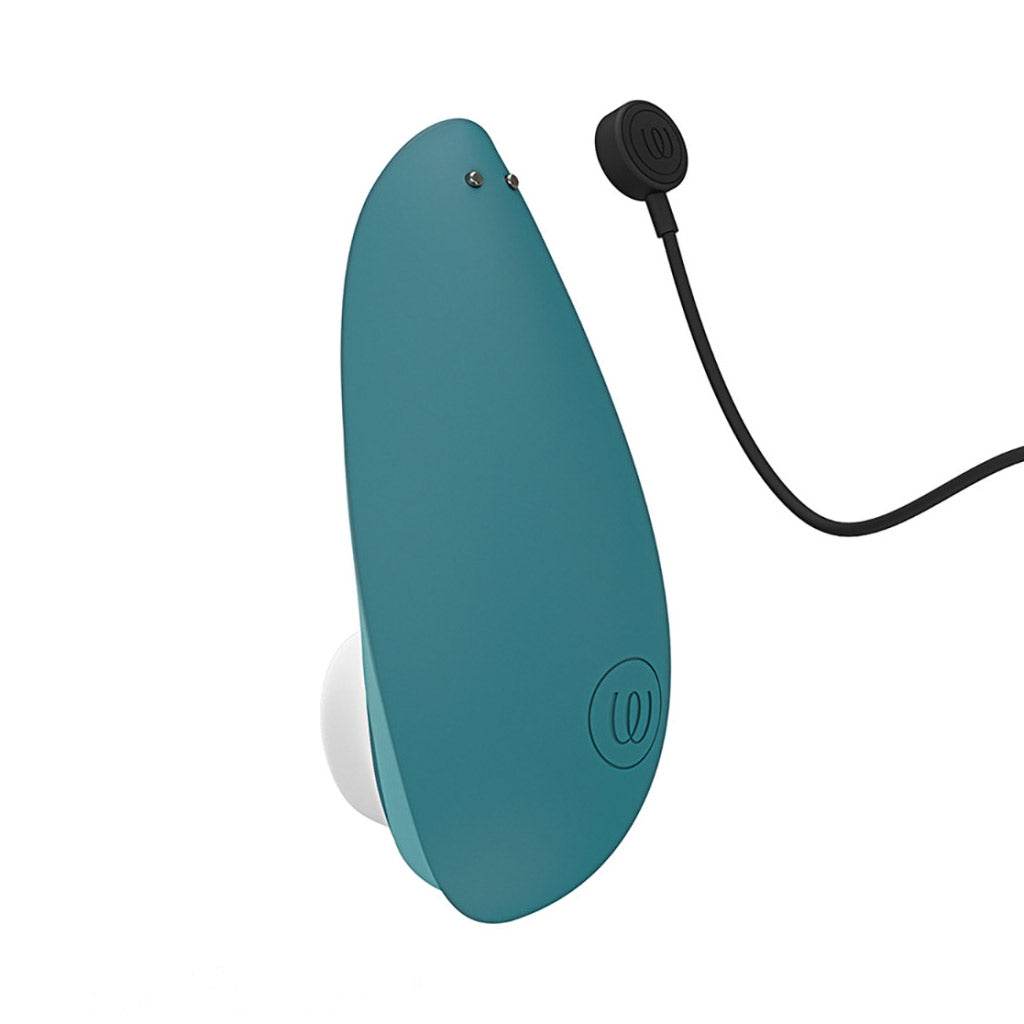 The backside of a teal Womanizer Liberty 2 vibrator, tilted to show the charging contact points. A black charging cord is coming from the right side. 