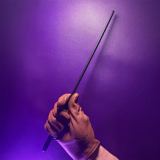 A black 12-inch Delrin cane is being heald by a hand wearing a tan leather glove against a purple leather background.
