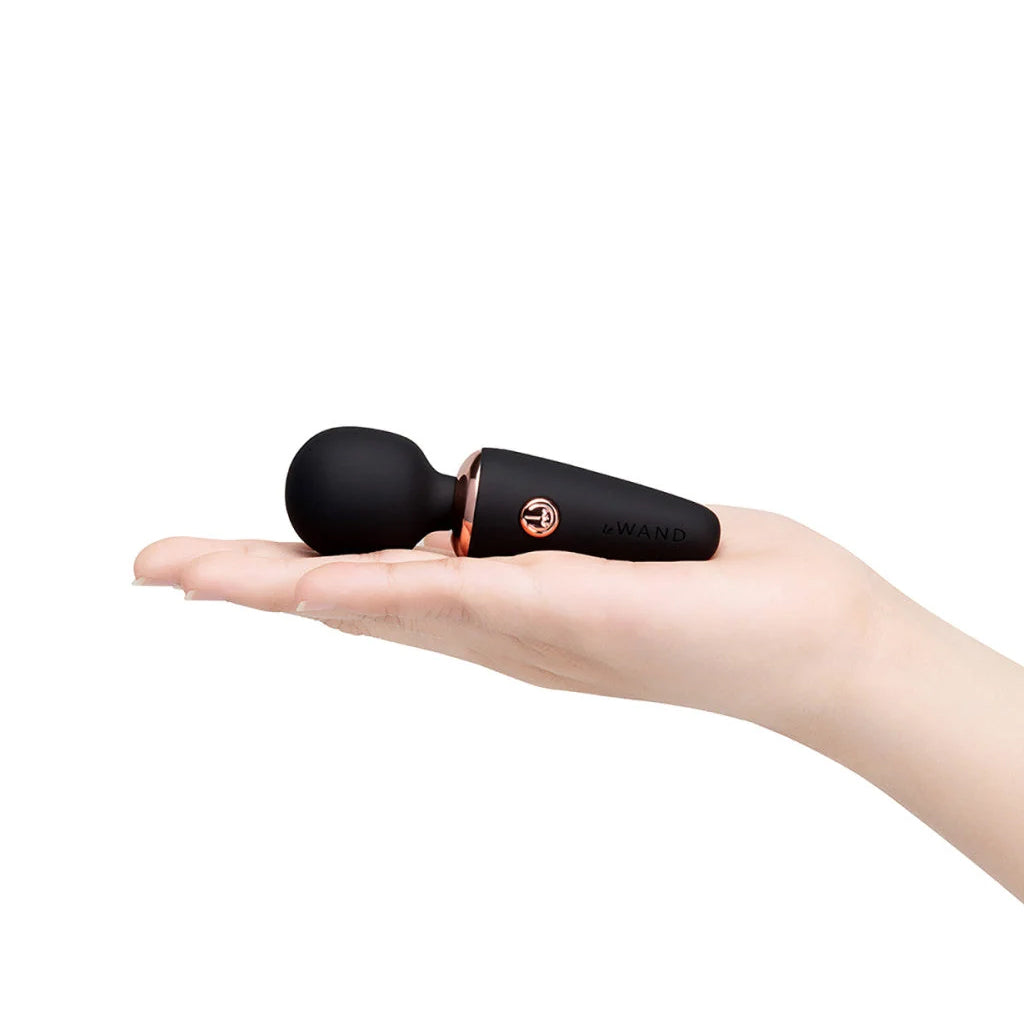 A hand is holding  the black Le Wand mini micro vibrator in their palm