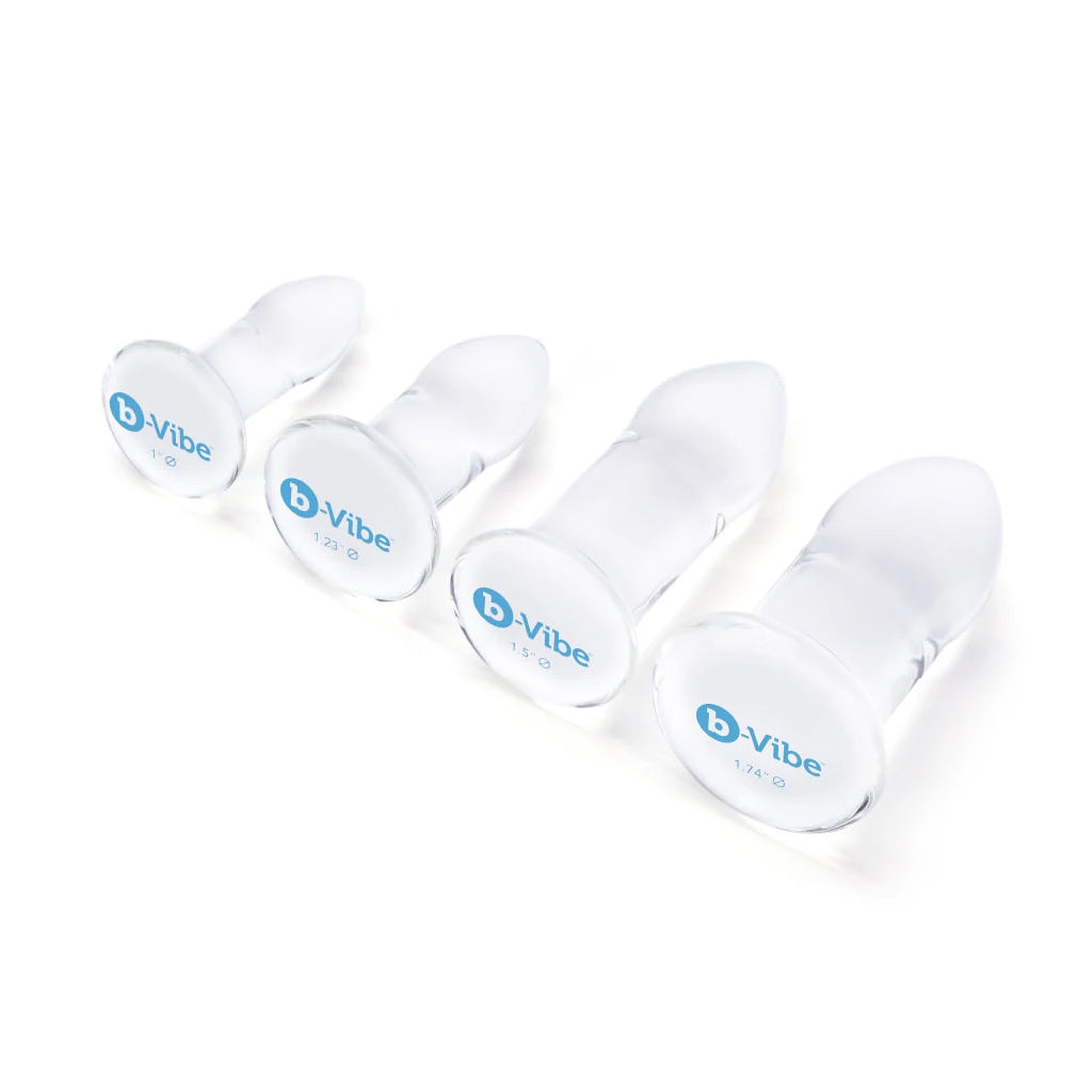The B-Vibe glass anal dilators 4 piece set is shown lying on its side on a white background. The B-Vibe logo can be seen at the bottom of the base in a baby blue color. 