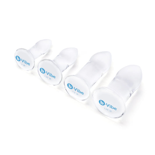 The B-Vibe glass anal dilators 4 piece set is shown lying on its side on a white background. The B-Vibe logo can be seen at the bottom of the base in a baby blue color. 