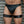 Load image into Gallery viewer, A close-up of a man&#39;s body from his waist to his knees is shown in front of a metal wall. He wears black leather underwear and Leather Thigh Cuffs, which are made of black leather and silver hardware. The cuffs have one small D-ring on the front.
