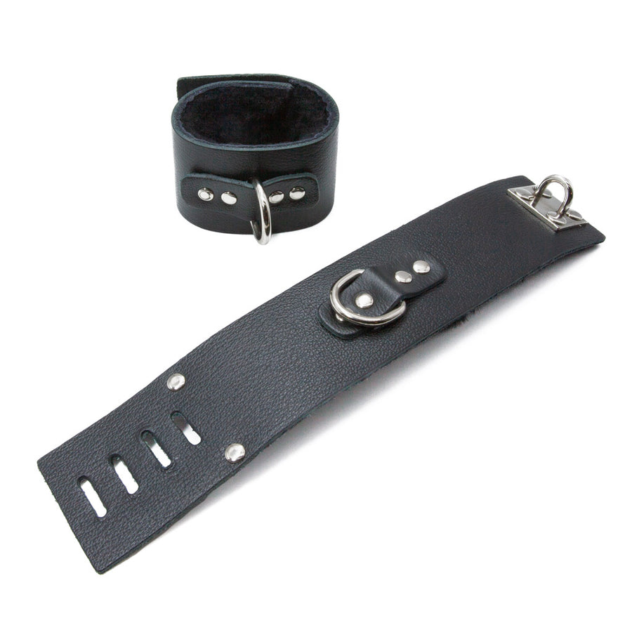 The Fleece-Lined Wrist Cuffs with a D-Ring, one cuffed and one uncuffed, are shown against a blank background. The cuffs are made of black leather and silver hardware, including a D-ring on each cuff. They are lined with black fleece.