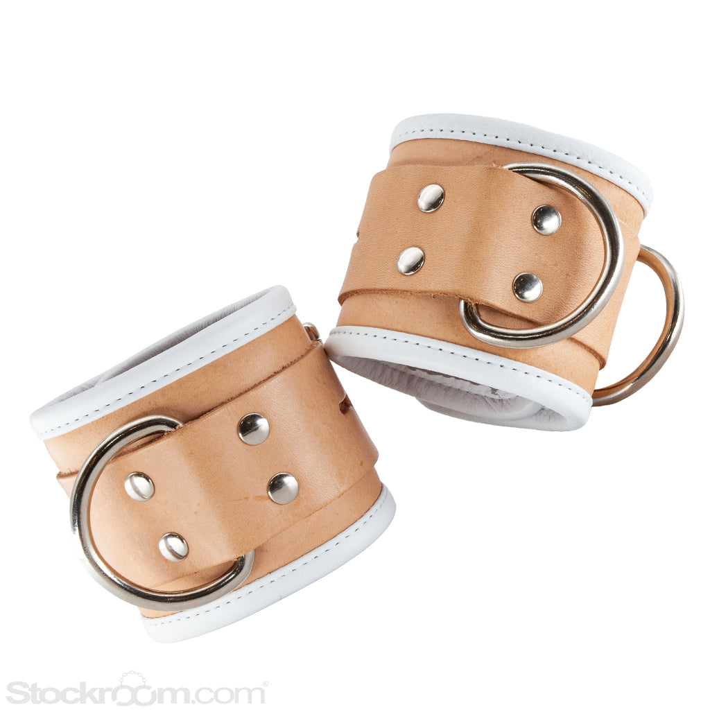 The Deluxe Padded Medical Leather Wrist Restraints are shown against a blank background. The cuffs are made of tan leather with a white border and a red inner lining. They have metal hardware.