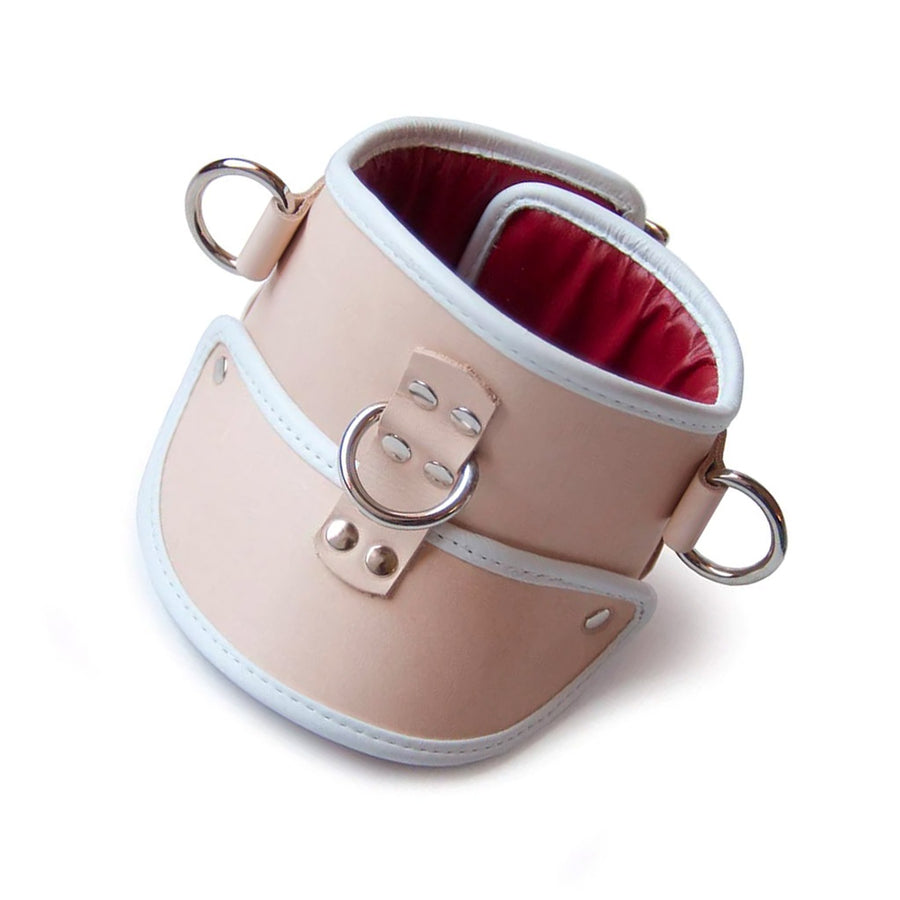 The Deluxe Padded Medical Leather Posture Collar is shown against a blank background. It is beige with white lining and silver hardware. The inner lining of the collar is red. There is a D-ring at the center and on each side of the collar.