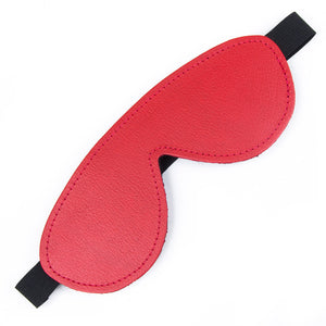 The red Fleece-Lined Leather Blindfold is shown against a blank background. It is made of red leather and shaped like goggles with a thick, black elastic strap.