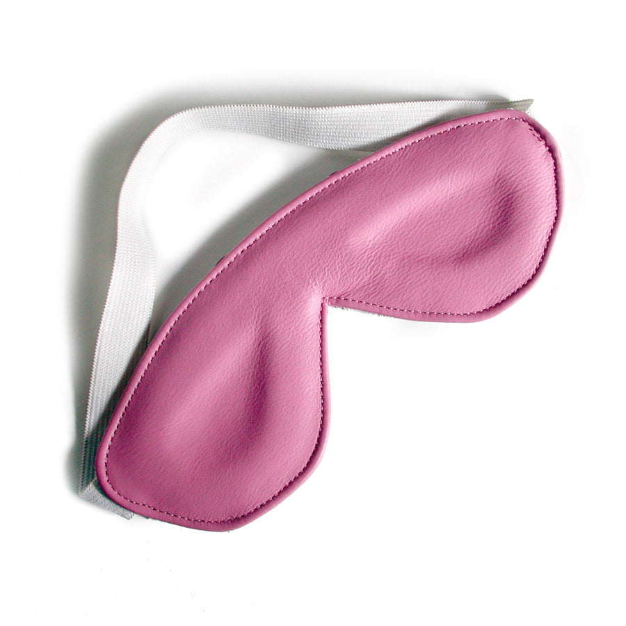 The Padded Pink Leather Blindfold is shown against a blank background. The blindfold is made of light pink leather and is shaped like goggles. It has a white elastic strap.