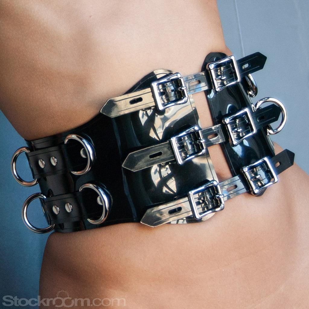 A close-up of a woman's waist in the Black PVC Waist Cincher is shown. The cincher has three adjustable straps in the center, each with two lockable buckles. There are four metal D-rings on each side.