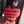 Load image into Gallery viewer, A dark-haired woman wearing the Red Bolero Straitjacket and a red leather thong is shown from behind. The jacket has rows of black leather adjustable straps that are secured with silver buckles.
