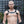 Load image into Gallery viewer, A man with a buzz cut and blonde facial hair stands in front of a black wall wearing the Bruiser Bulldog Leather Chest Harness. Black leather straps rest above his pecs and wrap under his arms and over his shoulders. The straps are connected with metal O-rings.
