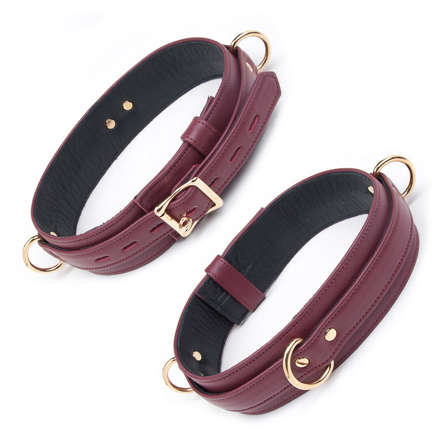 The JT Signature Collection Locking Thigh Cuffs are shown from the front against a blank background. It is made of Bordeaux leather with a black interior lining and gold hardware. There are three evenly spaced D-rings on the sides and center of the cuff.
