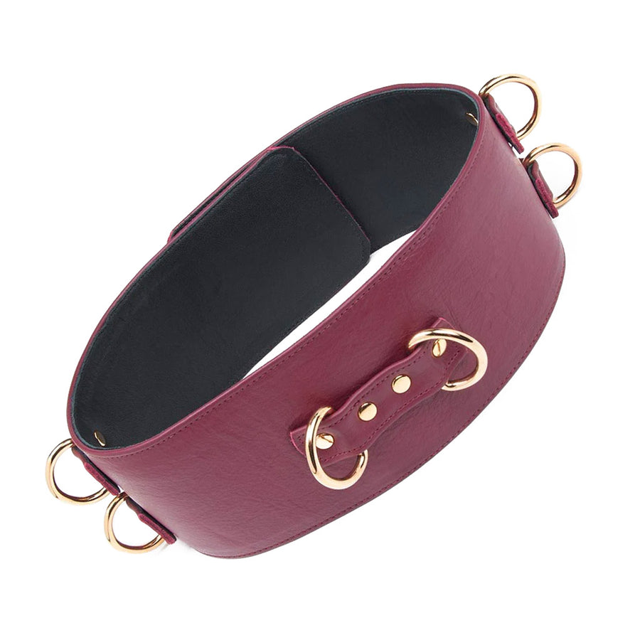 The JT Signature Collection Leather Waist Cuff is shown from the back against a blank background. It’s made of Bordeaux-colored leather with gold hardware. There are 2 D-rings near each other on the back of the cuff. Each side of the cuff has 2 D-rings stacked vertically.