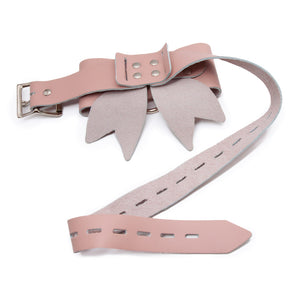 A product shot of the Stupid Cute Bow Restraint with the strap unfastened. It's made of light pink leather that comes together in a bow. There is a nickel-plated ring at the center of the bow. 