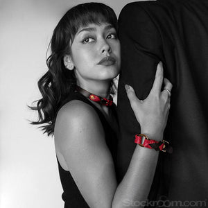 A black and white photo of a woman looking to the side with her arm holding a man's arm in a tuxedo. She is wearing the Melanie Rose Designs collar and wrist cuffs.