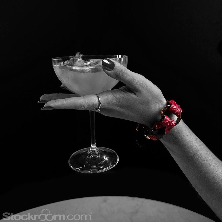 A woman’s forearm rests against a table and her hand is outstretched, holding a cocktail glass. The image is in black and white except for the Melanie Rose Designs x The Stockroom wrist cuff she is wearing.