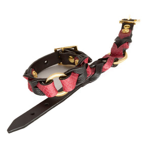 A pair of the Melanie Rose Designs x The Stockroom Wrist Cuffs, made of black and red leather braided together with a gold O-ring in the center, are displayed against a blank background.