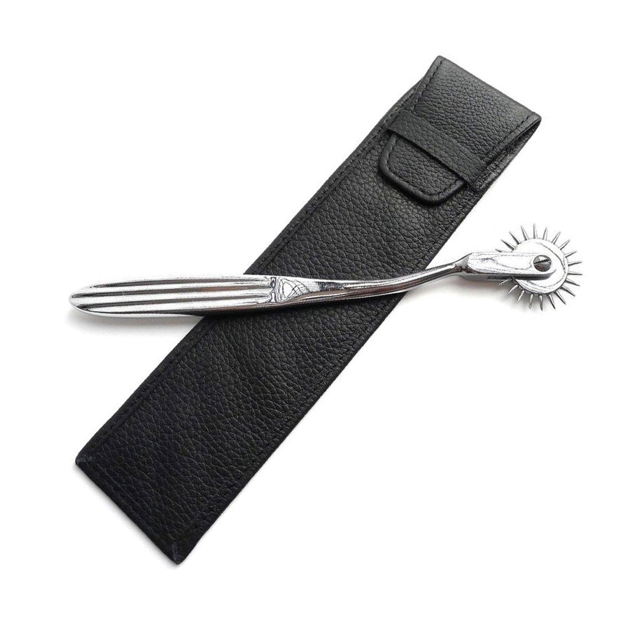 The KinkLab Wartenberg Pinwheel with Leather Sheath is displayed against a blank background. The pinwheel is made of silver metal with a single row of spikes. It rests on top of the case, made of black leather.