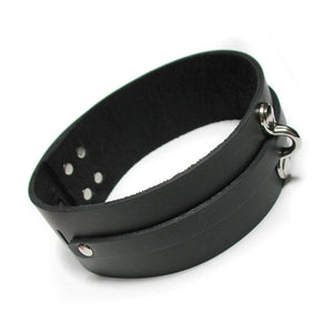 The KinkLab Bondage Basics Leather Collar is shown against a blank background. It is made of a wide piece of black leather with silver hardware. A thin leather strip runs along the middle of the collar and loops through a small D-ring.
