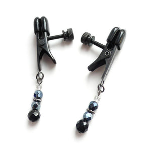 A pair of black Beaded Spring Jaw Nipple Clamps are displayed against a blank background. The clamps have rubber tips and a screw to adjust the tension, and each clamp has a string of beads dangling from the bottom.