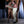 Load image into Gallery viewer, A brunette man with chest hair stands against a wooden beam. He is wrapped from his feet to under his pecs in Clear Latex Bondage Strips, making him resemble a mummy. A muscular nude man stands next to him and continues to wrap him.
