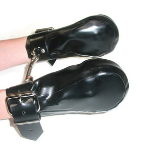 A person’s arms are held out in front of a white wall. Their hands are in the black Rubber Fist Mitts, which are black latex pouches with buckles around the wrists. The mitts each have a D-ring on the cuff, and they are hooked to each other with a snap hook.