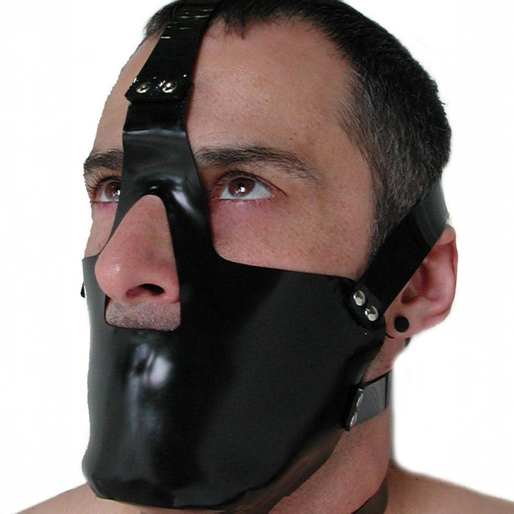 A close-up of a dark-haired man's face is shown against a blank background. He wears the rubber Head Harness with a Muzzle. It is a black muzzle that covers his mouth and chin and straps around his head.
