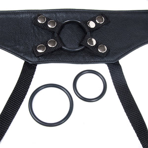 A close-up of the black leather Crown Strap-on harness is shown against a blank background. A medium-sized black rubber O-ring is attached to the harness, and one smaller and one larger O-ring are shown next to the harness.