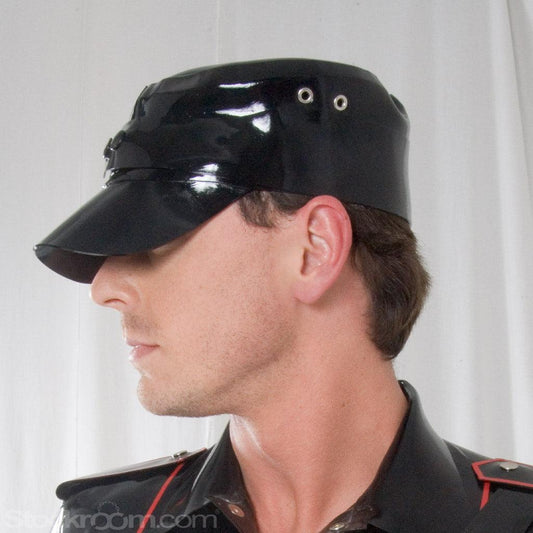 A headshot of a man in front of a white background. He wears the Rubber Soldier's Cap with Snaps by Syren Latex in black. The hat has a low brim and metal grommet accents on the sides.